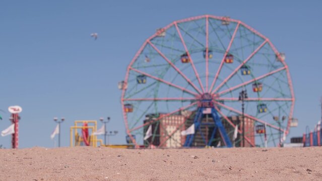 Coney Island sandy beach in Brooklyn, New York, United States. Boardwalk near retro luna park. Ferris wheel in american amusement park on ocean coast. Waterfront summer holiday promenade in NYC, USA.