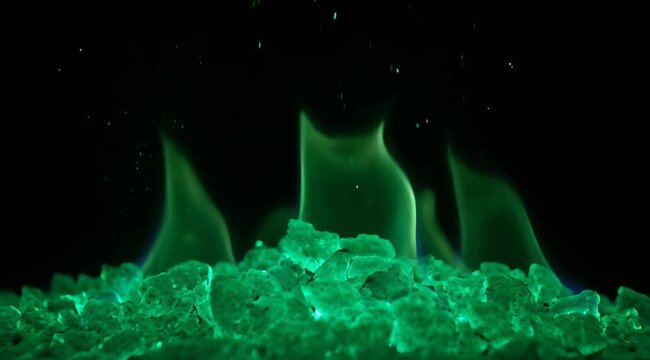 Close Up Of Green Flames Burning Above Emerald Glass Rocks In Darkness With Subtle Blue Highlights And Floating Embers