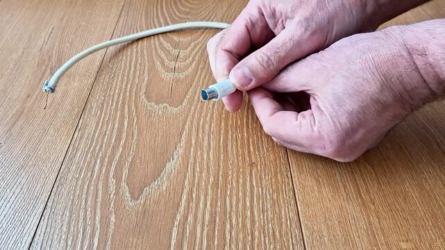 Close up of hands connecting a broken white cable on a wooden surface. Concept of repairing damaged electrical wires, DIY home maintenance, or fixing internet connection hardware