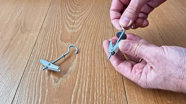 Toggle bolts displayed on a wooden surface with folded wings and threaded hook design, illustrating hardware components used for secure installation in hollow walls