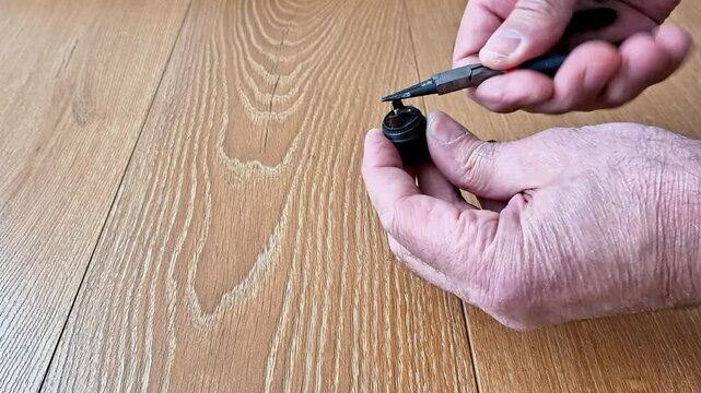 Hands using pliers to grip and adjust a small black hardware piece on a wooden surface, demonstrating precision work, repair technique, and practical DIY tool application