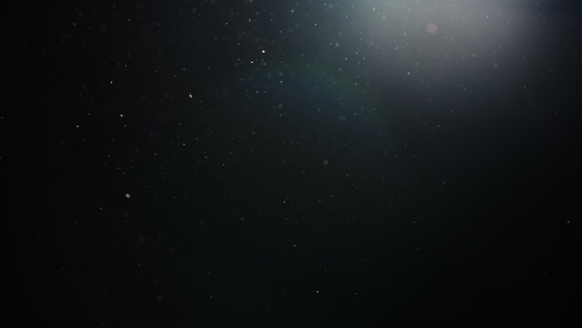 Slow motion real dust particles floating mid air over dark background