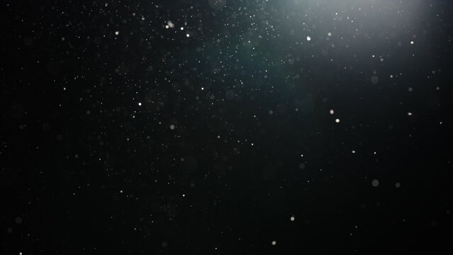 Slow motion real dust particles floating mid air over dark background