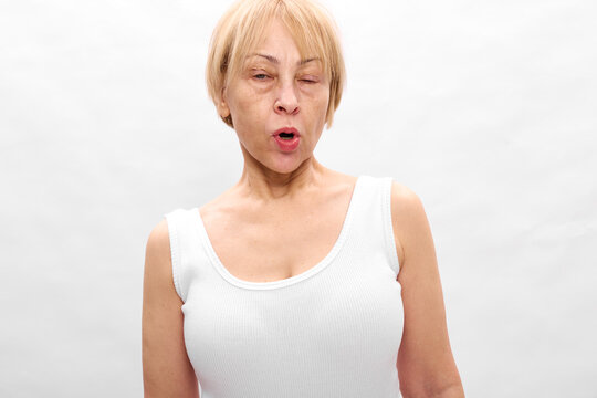 Woman blonde surprised mouth open tanktop white studio expression, older adult short hair, looking at camera, neutral light gray background, soft daylight