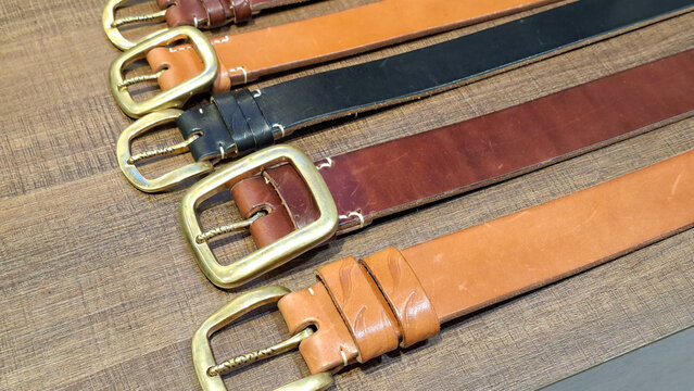 Row of Piger Works high quality genuine leather belts with brass buckles in various brown and black shades placed on wooden background on May 8, 2026 in Bangkok, Thailand.