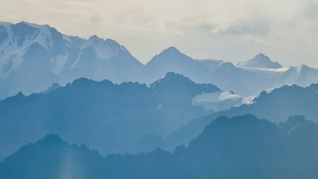 Artistic telephoto shot of distant mountain ridges creating blue layers of silhouettes under a soft sky. Minimalist mountain landscape.