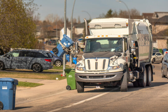 Calgary, Alberta, Canada. May 9, 2026. A white City of Calgary waste management truck lifts a blue recycling bin in a sunny neighborhood.