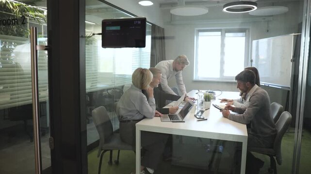 Group of business people standing together and discussing their work and projects, having a team meeting in an office, view from glass wall