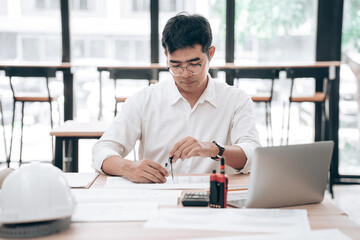 Fototapeta premium Young male architect or engineer reviewing blueprints at desk in modern office