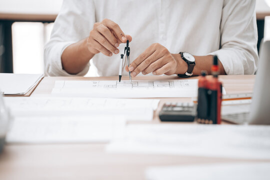 Architect or engineer drawing on technical blueprint with drafting tools in office