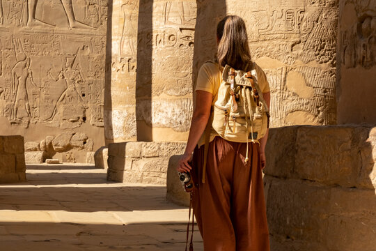 Visitor explores ancient Egyptian temple while studying hieroglyphs on the walls during daylight hours. 