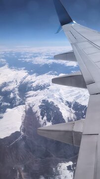 Wing over rugged snowy mountain valley with sweeping panorama jagged peaks and glacier rivers under clear blue sky, crisp contrast