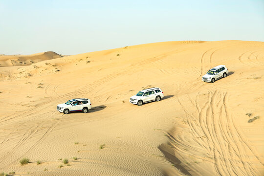White SUV Driving Across Murqquab Desert Dunes at Sunset, Dubai, United Arab Emirates