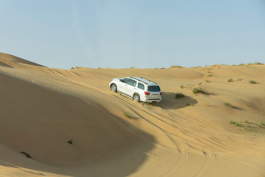White SUV Driving Across Murqquab Desert Dunes at Sunset, Dubai, United Arab Emirates