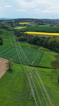 Aerial view flying along power lines over green countryside fields