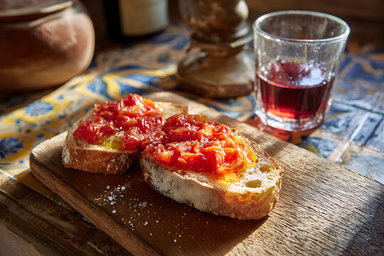 Rustic tomato bruschetta with salt and olive oil on a wooden board in the sunlight.