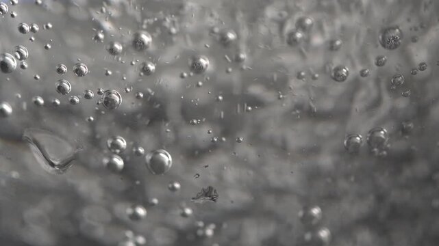 Many small bubbles in a glass of water in macro view on a light background, bubbles in a glass