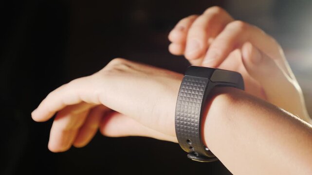 A person uses their smartwatch in a medium close-up shot, showcasing interaction with the wearable technology in a dimly lit setting.