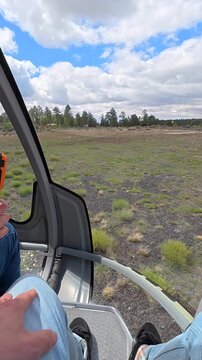 Passenger's point of view from a helicopter taking off from the runway at grand canyon national park airport, showing the ground getting farther away and the beautiful cloudy sky above