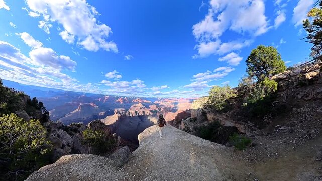 Young smiling hiker woman walking along a dangerous cliff edge at grand canyon national park, enjoying the stunning panoramic view and making a heart shape with her hands toward the camera