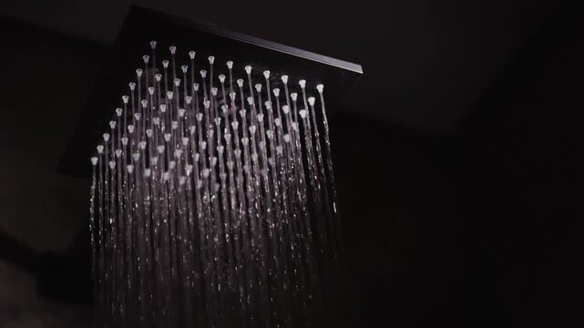 Square rainfall shower head releasing water stream in modern bathroom.