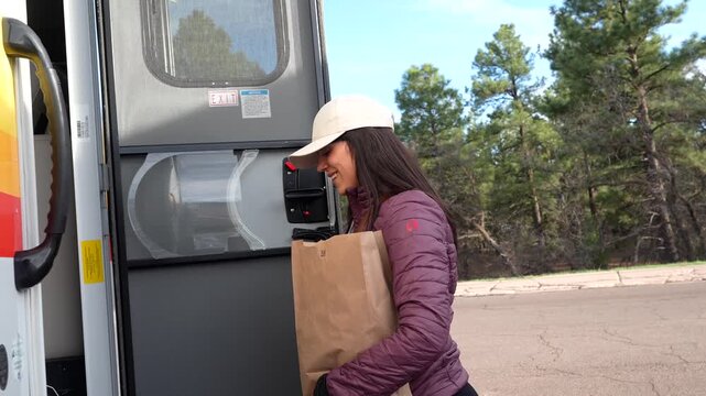 Young smiling woman carrying a paper bag getting on a public shuttle bus in grand canyon national park, arizona, ready for a day of hiking and exploring the famous bright angel trailhead