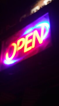 Bright red and blue neon sign with the word open flashing at night, illuminating a dark storefront and signaling that the business is ready for customers and commerce is active