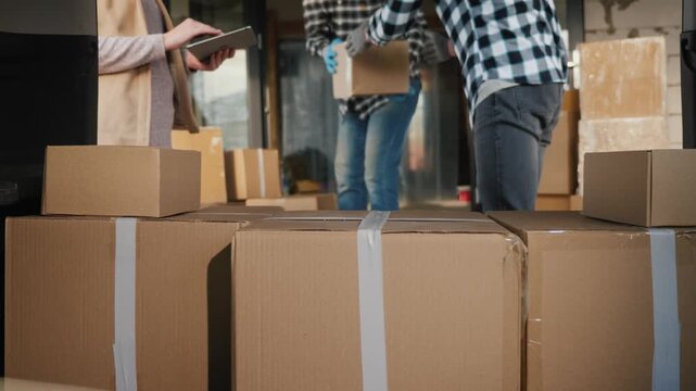 Team of professional loaders and logistics manager working together while loading cardboard boxes into delivery van truck.