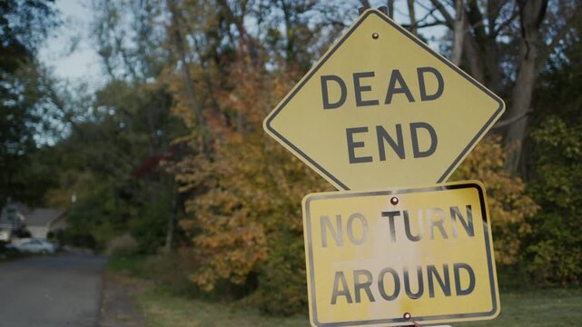 Dead end and no turn around road signs in suburban area with trees and houses in the distance.