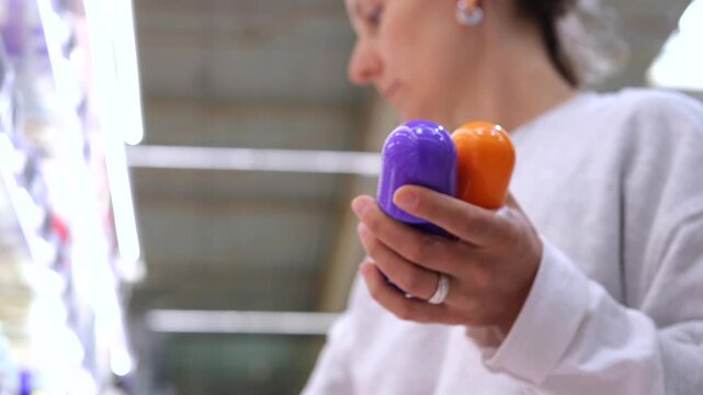 Young woman shopping in a store's personal care aisle, carefully selecting a deodorant from the shelf and examining the products before making a purchase, focused on making the right choice