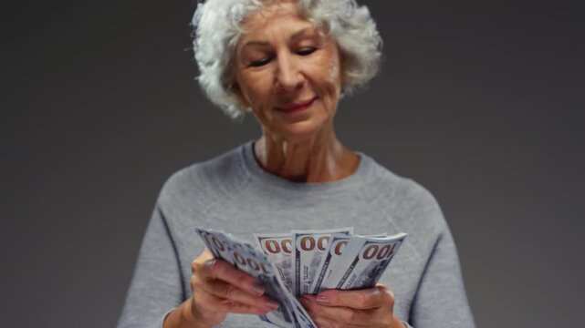 Grandmother counting paper cash. Senior female holding bundle of USD money in hands and throwing one hundred 100 dollar bills. Arms of old woman flipping through currency. Grey hair, wrinkled fingers