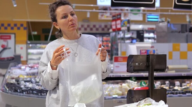 Frustrated female customer trying to open a flimsy plastic produce bag in a grocery store while shopping for food, showing the inconvenience of single use packaging during daily errands