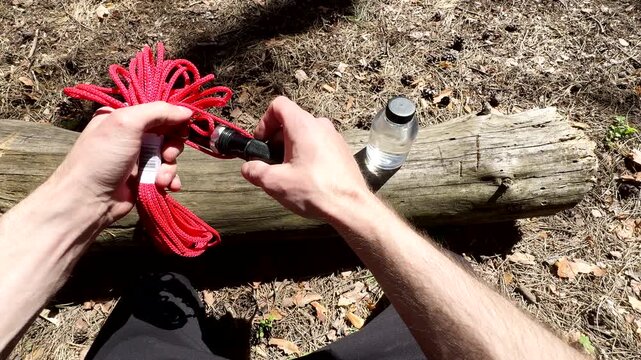 POV of a man laying out essential survival gear on a log. Hand placing a knife, flashlight, rope, metal cup, and water bottle. Bushcraft and wilderness preparation concept