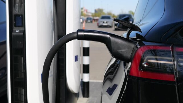 Modern black electric vehicle plugged into a fast charging station with a power cable at a public supercharger network, refueling its battery for clean, sustainable transportation