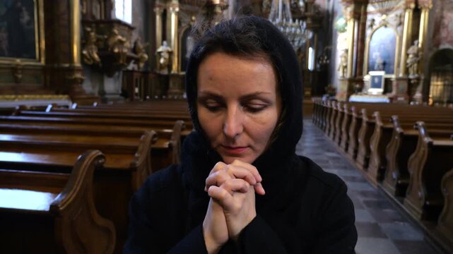 Devout christian woman with her hands clasped together in prayer, seeking solace and forgiveness inside an old, empty catholic church. Her deep faith is reflected in her peaceful contemplation