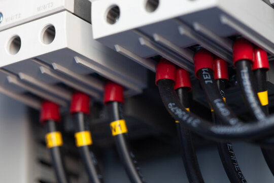 Professional close-up view of a modern industrial electrical control panel interior featuring neatly organized wiring, red and black cables with ferrules, terminal blocks, and modular contactors/break