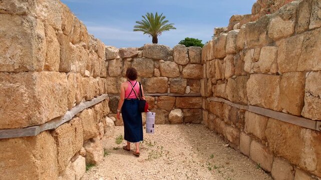 Female tourist standing among ancient stone wall excavations at Tel Megiddo National Park in Israel. Woman traveler holds a map while exploring the historical archaeological site in Jezreel Valley