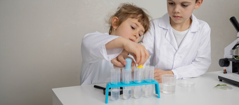 Children scientists examining water sample with magnifying glass in lab