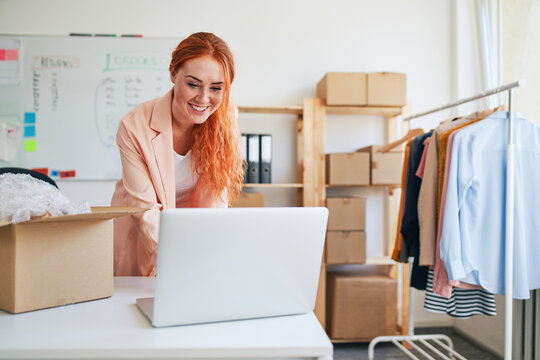 Young woman managing online clothing shop at laptop in warehouse