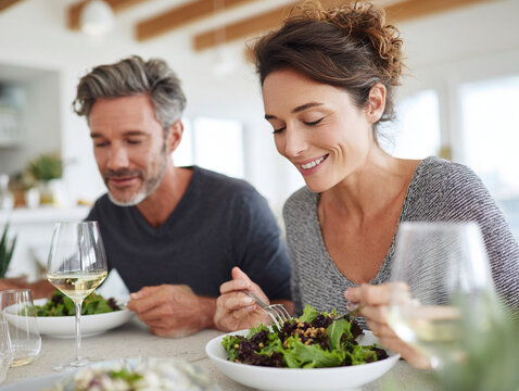 Joyful young couple enjoying meal together at home, savoring fresh salads and white wine in stylish kitchen. Their connection and happiness are evident as they share this moment