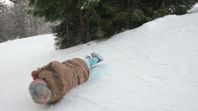 Young girl rolling down snowy hill in mountains.