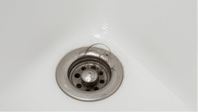 Close-up of a clogged bathroom sink drain filled with tangled hair, indicating the need for cleaning.