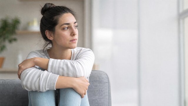sad woman sitting on couch looking out window