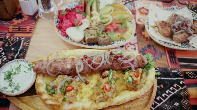 Georgian kebab platter with traditional pickles and khachapuri served on ethnic tablecloth in cafe.