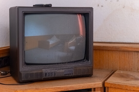Old television resting on wooden surface, dust covering its surface, evoking memories of past entertainment in a forgotten room