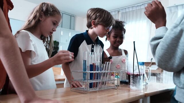 A group of boys and girls of various nationalities stand in front of their classmates learning science, mixing chemicals and holding test tubes in their classroom at school.
