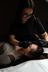 Obraz premium Esthetician with gloves applying permanent makeup on woman's eyebrows for cosmetic beauty