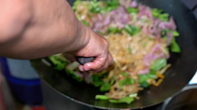 Flat rice noodles stir-fried with beef and green vegetables in a hot wok, close-up Asian street food cooking