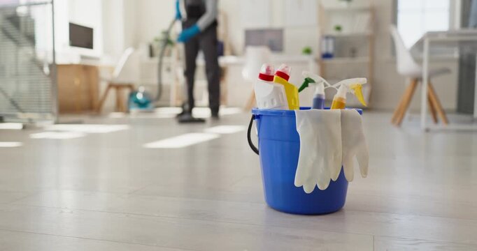 Cleaner mopping office floor with bucket and supplies. Blue bucket holds spray bottles and gloves on bright laminate in a modern office workspace. Clean office hygiene and cleaning service.