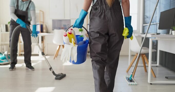 Janitor cleaner worker cleaning office with supplies. Back view of staff carrying a bucket with gloves across a bright workplace. Highlights reliable office hygiene and professional cleaning.